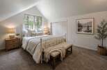 Experience serene living in this charming bedroom, featuring a vaulted ceiling and a large window that floods the space with natural light and offers picturesque forest views.