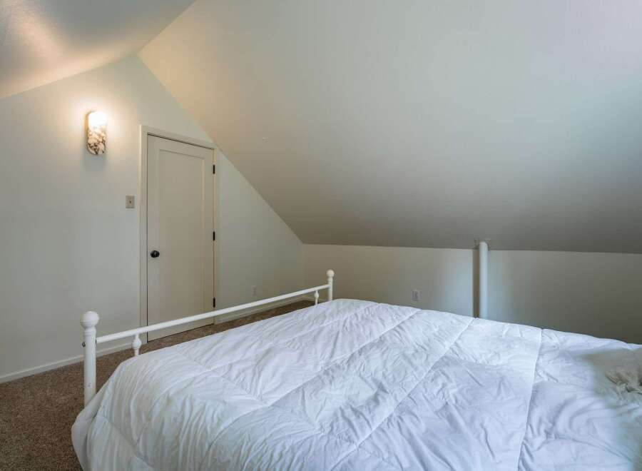 Discover cozy charm in this attic bedroom, featuring a comfortable white comforter on a classic metal bed frame.