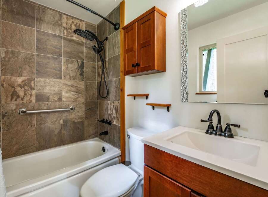 This updated bathroom features a stylish tiled shower and tub surround, complemented by a modern black showerhead and fixtures.