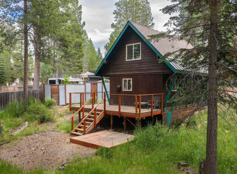 Charming A-frame cabin nestled amongst tall pine trees, featuring a spacious wooden deck perfect for outdoor entertaining.