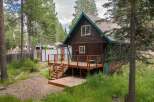 Charming A-frame cabin nestled amongst tall pine trees, featuring a spacious wooden deck perfect for outdoor entertaining.