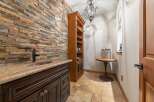 This stylish wet bar area features a striking stacked stone accent wall, complemented by a granite countertop and a dark wood vanity with ornate hardware.