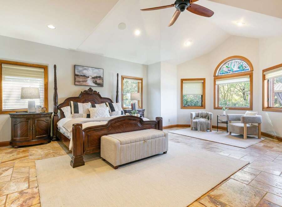 Experience luxury in this spacious master bedroom featuring a grand four-poster bed and a charming seating area by the arched stained-glass window.