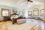 Experience luxury in this spacious master bedroom featuring a grand four-poster bed and a charming seating area by the arched stained-glass window.