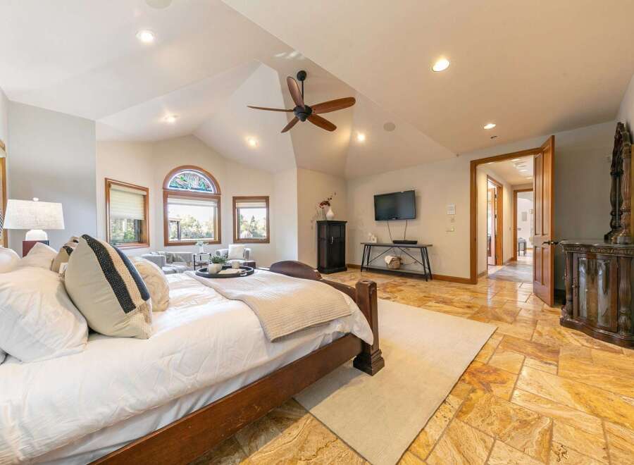 Experience luxury in this spacious master suite, featuring a grand four-poster bed and a cozy seating area by the arched stained-glass window.