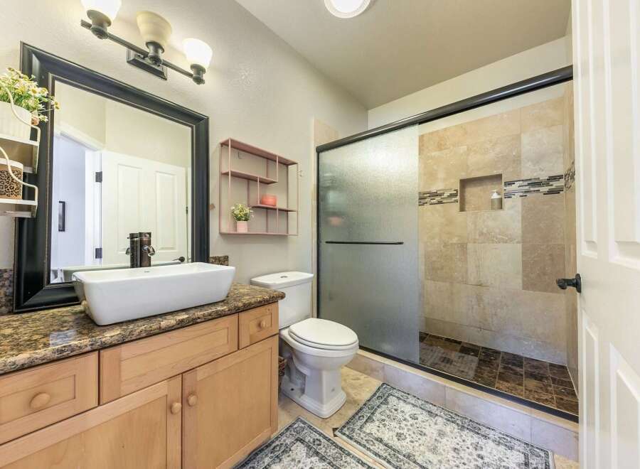 This modern bathroom features a spacious vanity with a vessel sink and granite countertops, complemented by a large framed mirror.