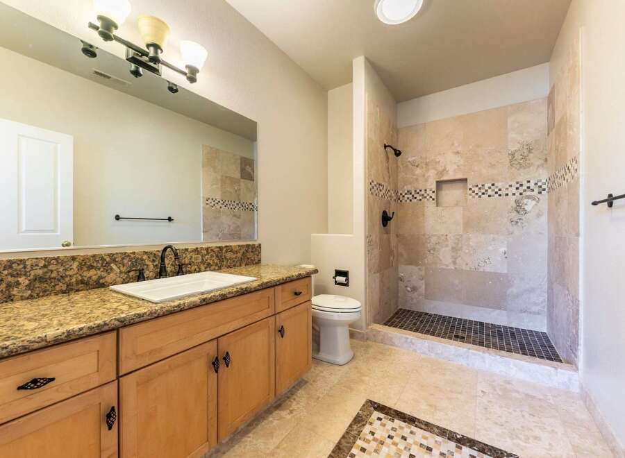 This beautifully appointed bathroom features a spacious vanity with granite countertops and ample storage, complemented by a large mirror and elegant light fixture.