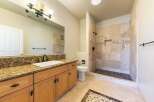 This beautifully appointed bathroom features a spacious vanity with granite countertops and ample storage, complemented by a large mirror and elegant light fixture.