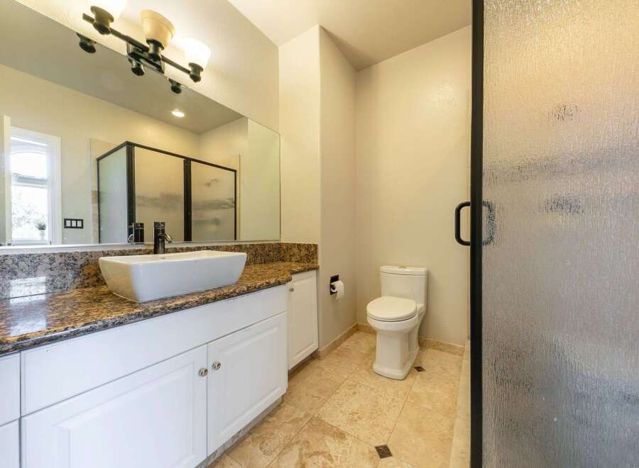 This spacious bathroom features a modern vessel sink atop a granite countertop with ample storage below.