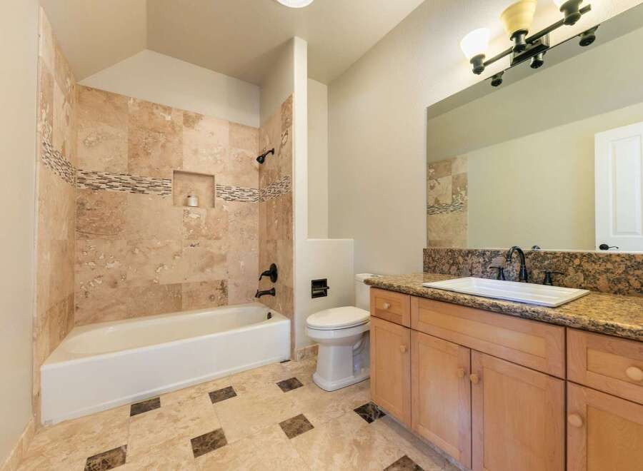 This beautifully appointed bathroom features a luxurious travertine tile shower and bathtub surround, complemented by a decorative mosaic tile accent.