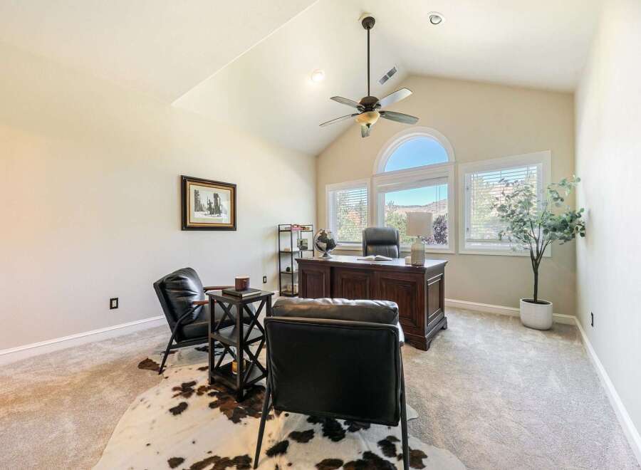 This executive home office features a grand wooden desk with a leather chair, complemented by two plush leather armchairs and a striking cowhide rug.