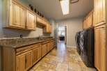 This spacious laundry room features ample natural wood cabinetry providing abundant storage, complemented by a granite countertop and a deep sink.