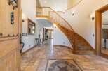 Step into this grand foyer featuring a stunning curved staircase with rich wooden railings and a decorative compass rose inlay on the travertine tile floor.