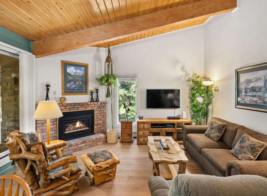 Cozy up by the brick fireplace in this inviting living room, featuring rustic log furniture and a beautiful wooden ceiling.
