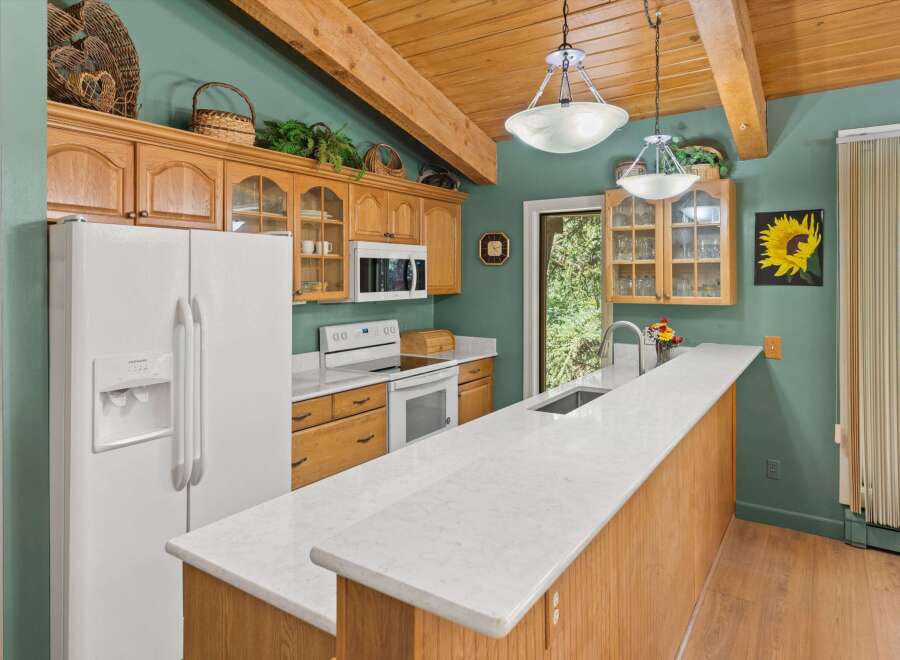 Discover this charming kitchen featuring warm wooden cabinetry and a spacious quartz countertop island, perfect for meal preparation and casual dining.