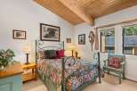 Experience rustic charm in this cozy bedroom, featuring a beautiful floral comforter on a wrought-iron bed and a vaulted wood-paneled ceiling with exposed beams.