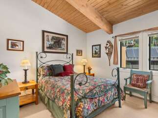 Experience rustic charm in this cozy bedroom, featuring a beautiful floral comforter on a wrought-iron bed and a vaulted wood-paneled ceiling with exposed beams.