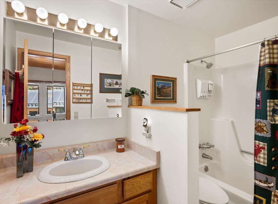 This charming bathroom features a spacious vanity with a marble-look countertop and a large mirror with overhead lighting.
