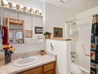 This charming bathroom features a spacious vanity with a marble-look countertop and a large mirror with overhead lighting.