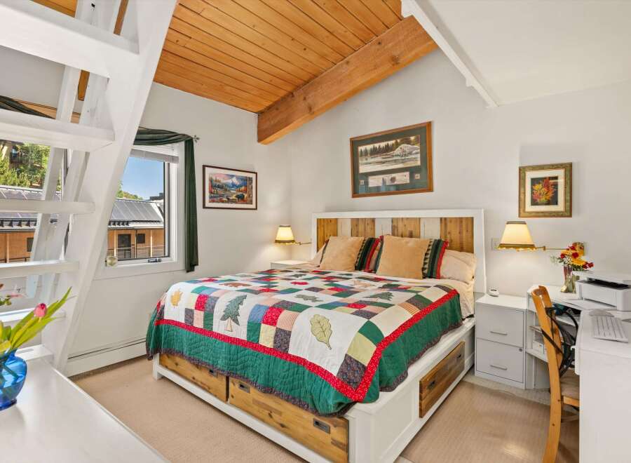 Experience cozy comfort in this charming bedroom featuring a rustic wooden headboard and a vibrant, nature-themed quilt.