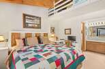Experience rustic charm in this cozy bedroom featuring a unique wooden headboard and a colorful, nature-themed quilt.