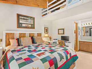 Experience rustic charm in this cozy bedroom featuring a unique wooden headboard and a colorful, nature-themed quilt.
