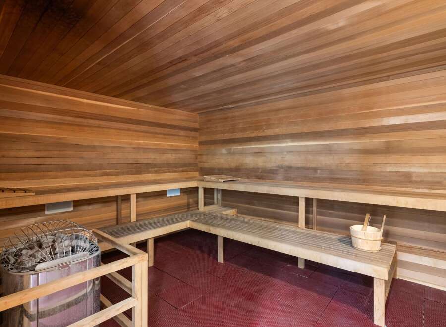 Experience ultimate relaxation in this luxurious wooden sauna, featuring ample seating and a modern heater with stones.