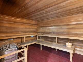 Experience ultimate relaxation in this luxurious wooden sauna, featuring ample seating and a modern heater with stones.