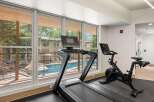 Elevate your fitness routine in this modern gym, featuring a treadmill and a Peloton bike with stunning views of the outdoor pool and surrounding trees.