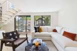Experience modern living in this bright and airy space, featuring a sleek white sectional sofa complemented by accent pillows and a unique knot pillow.