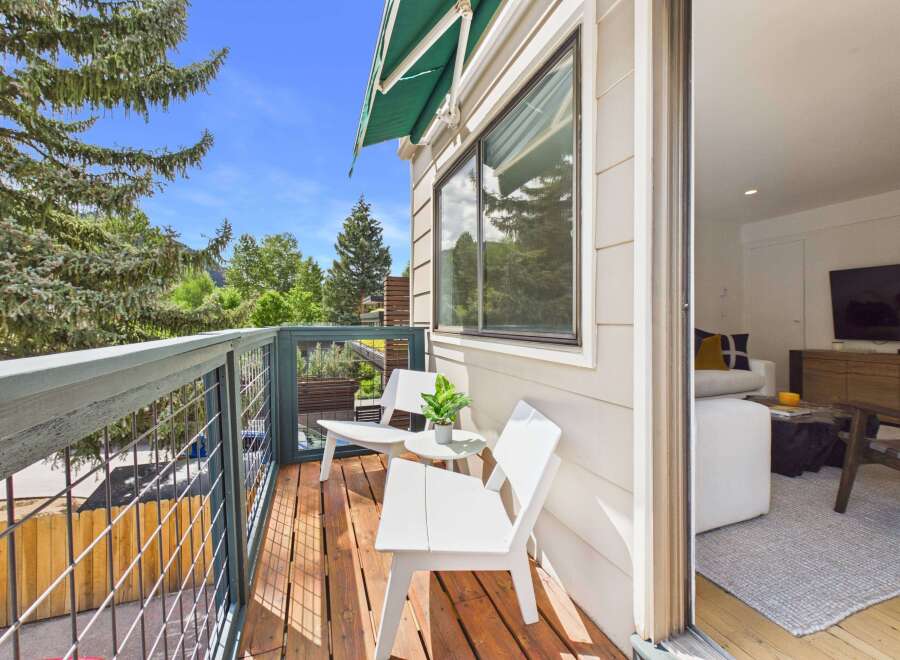 Enjoy your morning coffee on this charming balcony, complete with two white chairs and a small table, offering a perfect spot to relax amidst the lush greenery.