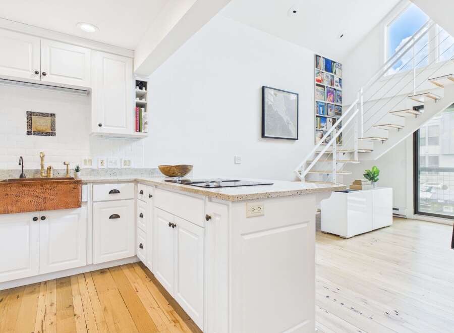 Experience modern living in this bright and airy kitchen featuring crisp white cabinetry, a stunning copper farmhouse sink, and a sleek granite countertop island with a built-in stovetop.