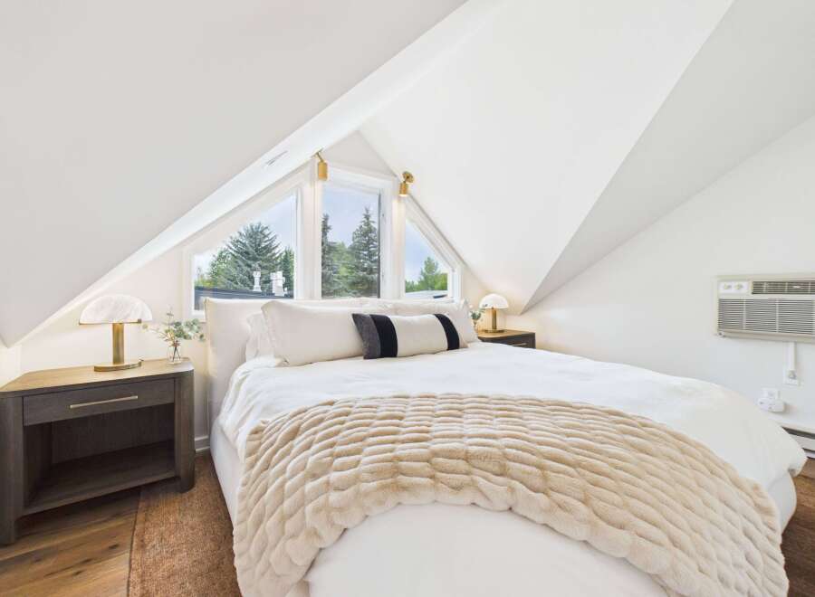 Experience serene comfort in this charming attic bedroom, featuring a plush bed adorned with a cozy throw and accent pillows.