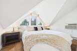 Experience serene comfort in this charming attic bedroom, featuring a plush bed adorned with a cozy throw and accent pillows.