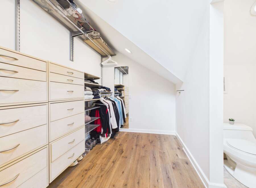 Discover this spacious walk-in closet featuring ample storage with light wood drawers and shelving.
