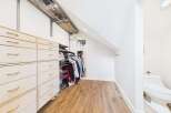 Discover this spacious walk-in closet featuring ample storage with light wood drawers and shelving.