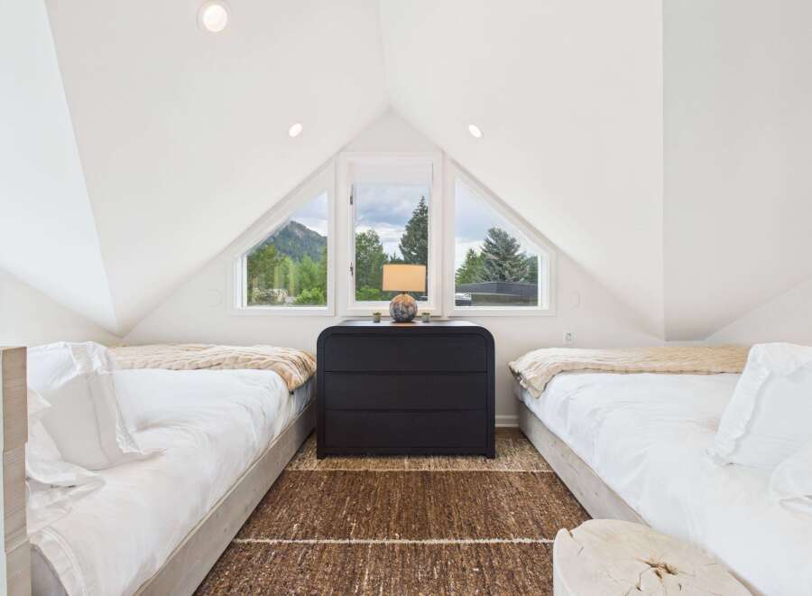 Experience breathtaking mountain views from this charming attic bedroom, featuring two cozy beds and a unique triangular window.