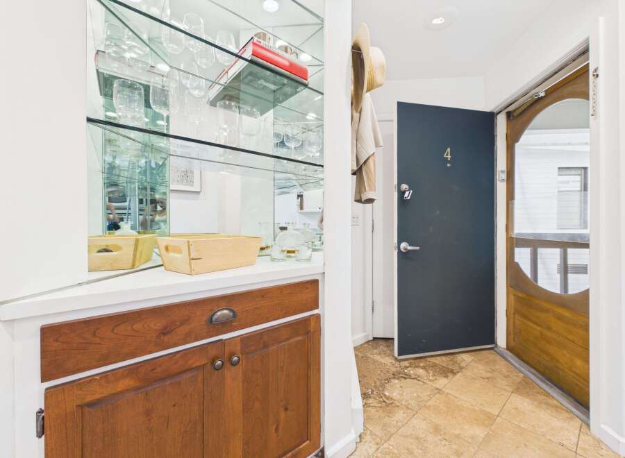 Step into this charming entryway featuring a mirrored bar area with ample glassware and a wooden cabinet for storage.