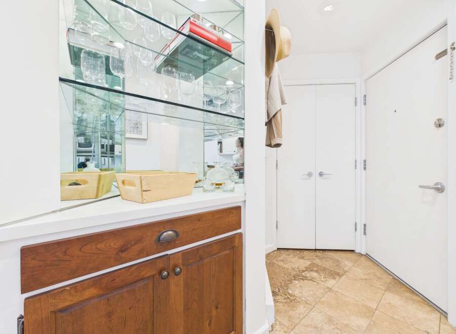 This entryway features a mirrored wall with glass shelving displaying glassware, creating a sense of spaciousness and elegance.