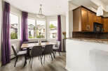 Bright and airy dining area featuring a modern wooden table with upholstered chairs and a bench, complemented by elegant purple sheer curtains framing large windows.