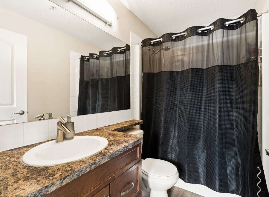 This bathroom features a modern vanity with a granite countertop and a sleek faucet, complemented by a large mirror and a white tiled backsplash.