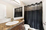 This bathroom features a modern vanity with a granite countertop and a sleek faucet, complemented by a large mirror and a white tiled backsplash.