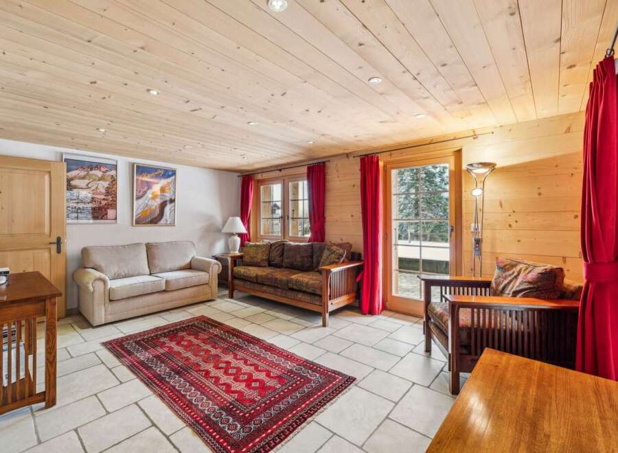 Experience cozy living in this charming room featuring a warm wooden ceiling and walls, complemented by a plush red rug.