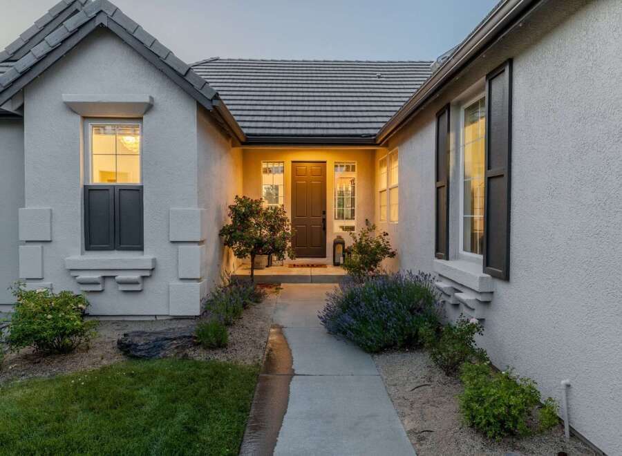 Welcome guests to this charming home with a beautifully lit entryway, featuring a classic dark brown door flanked by elegant windows.