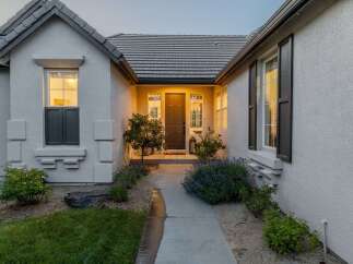 Welcome guests to this charming home with a beautifully lit entryway, featuring a classic dark brown door flanked by elegant windows.