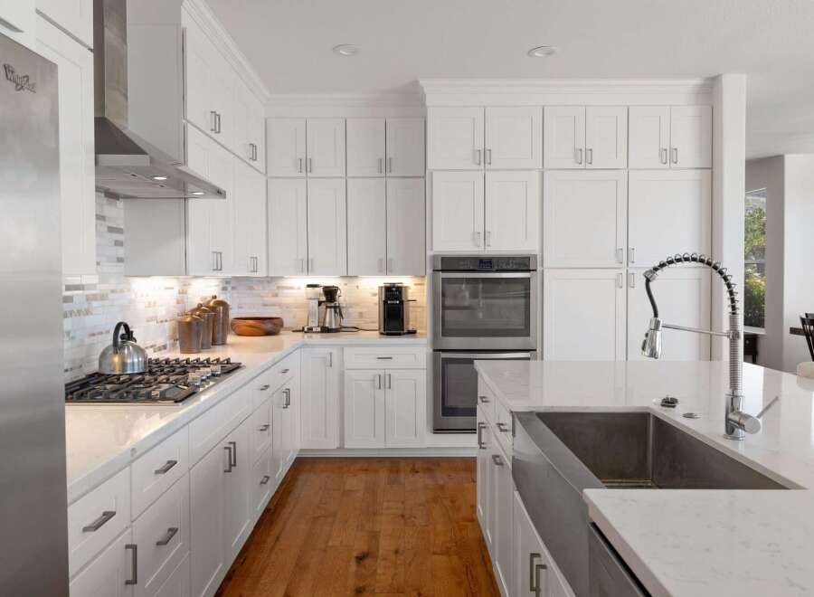 This stunning white kitchen boasts modern stainless steel appliances, including a built-in oven and a sleek gas range with a stylish backsplash.