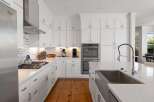 This stunning white kitchen boasts modern stainless steel appliances, including a built-in oven and a sleek gas range with a stylish backsplash.