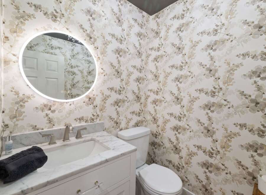 This powder room features a stylish vanity with a marble countertop and a sleek faucet, complemented by a round, illuminated mirror.