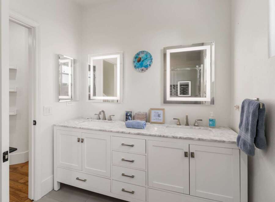 This modern bathroom features a spacious double vanity with a marble countertop, illuminated mirrors, and sleek chrome fixtures.