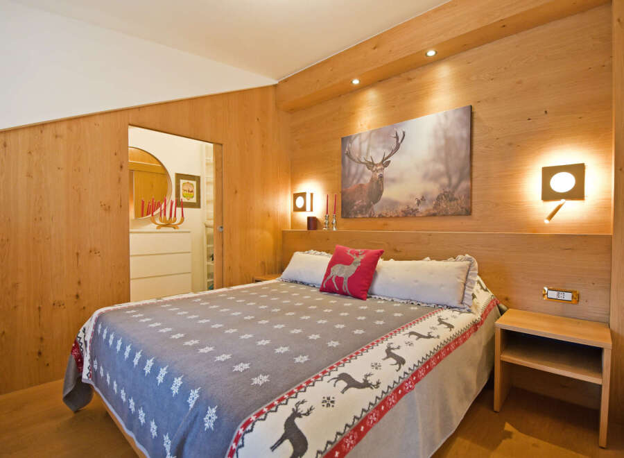 Experience rustic charm in this beautifully appointed bedroom, featuring warm wood paneling and a cozy queen-sized bed adorned with a festive reindeer-themed blanket.